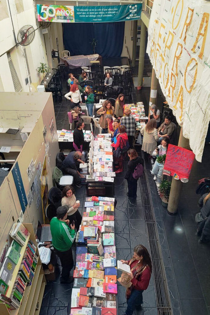 Patio del instituto, visto desde arriba, con mesas llenas de libros y personas recorriendo.